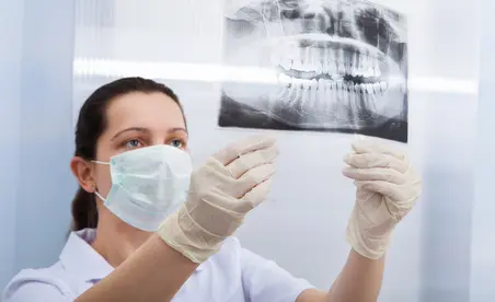 Eine Zahnärztin in Schutzkleidung betrachtet aufmerksam ein dental-radiografisches Bild.